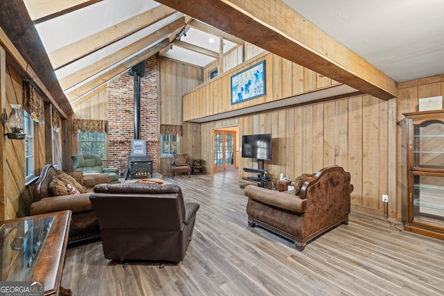 living room featuring beamed ceiling, wood-type flooring, a wood stove, and wooden walls