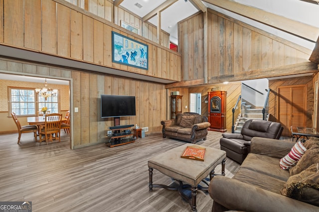 living room with high vaulted ceiling, a chandelier, wooden walls, and light hardwood / wood-style flooring