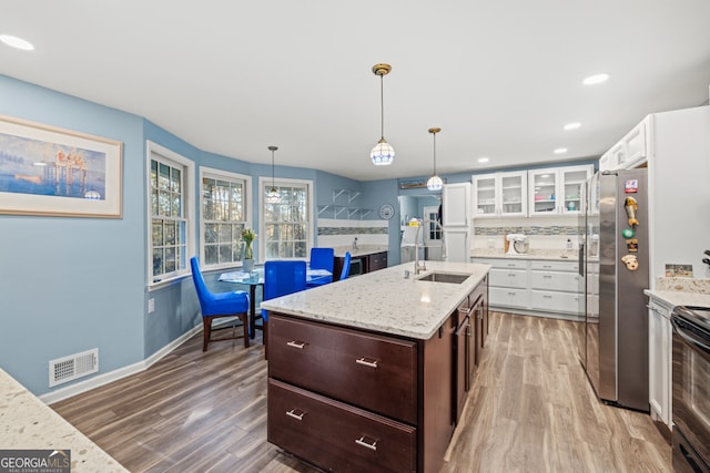 kitchen featuring sink, stainless steel fridge, wood-type flooring, a kitchen island with sink, and white cabinets