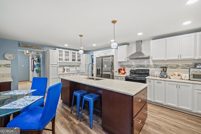 kitchen featuring white cabinets, black range with electric stovetop, wall chimney range hood, stainless steel refrigerator with ice dispenser, and light hardwood / wood-style flooring