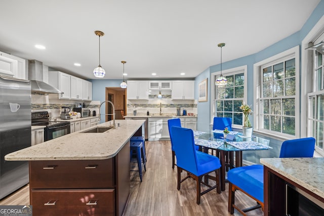 kitchen featuring white cabinetry, sink, wall chimney range hood, black / electric stove, and decorative light fixtures