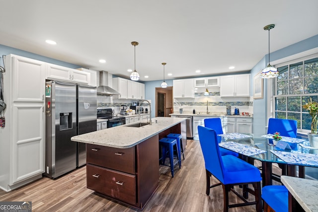 kitchen with appliances with stainless steel finishes, wall chimney exhaust hood, sink, wood-type flooring, and white cabinetry