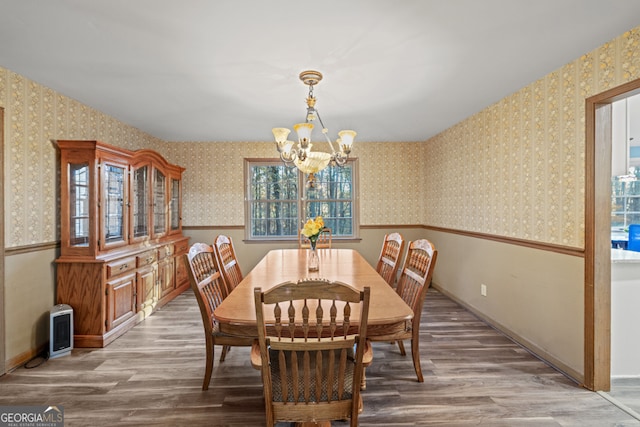 dining space with heating unit, a wealth of natural light, wood-type flooring, and an inviting chandelier