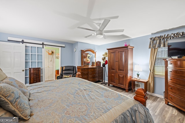 bedroom with a barn door, light hardwood / wood-style floors, and ceiling fan