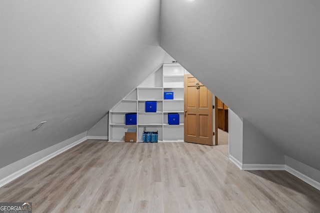 additional living space featuring built in shelves, vaulted ceiling, and light hardwood / wood-style flooring