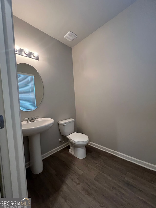 bathroom with toilet, a sink, wood finished floors, visible vents, and baseboards