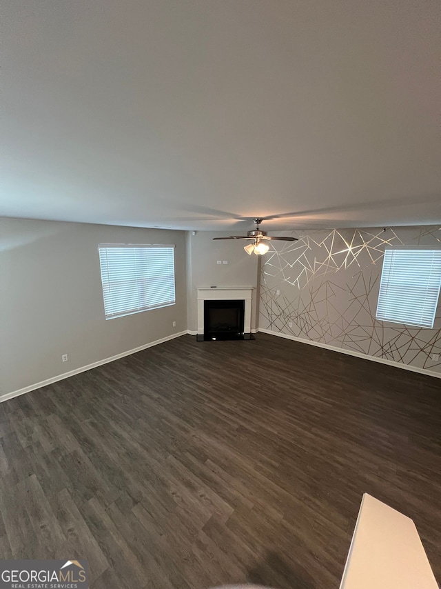 unfurnished living room with dark wood-style floors, a fireplace, baseboards, and a ceiling fan