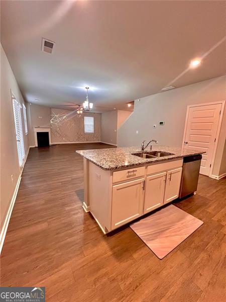 kitchen featuring wood finished floors, a sink, white cabinets, open floor plan, and a center island with sink