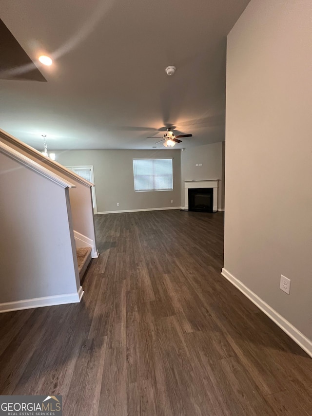 unfurnished living room with dark wood-style flooring, a fireplace, stairway, ceiling fan, and baseboards