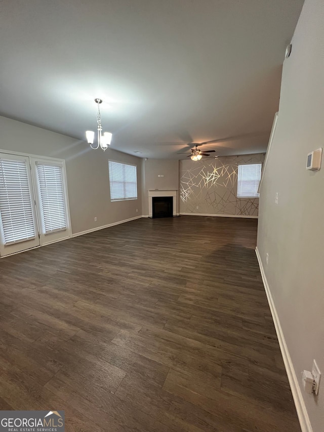 unfurnished living room with dark wood-type flooring, a fireplace, baseboards, and ceiling fan with notable chandelier