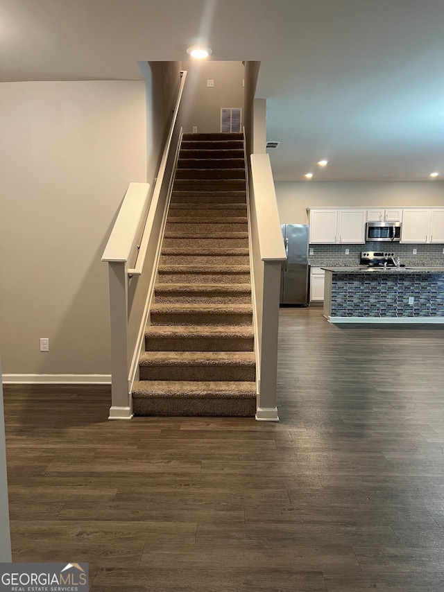 stairway featuring baseboards, wood finished floors, visible vents, and recessed lighting