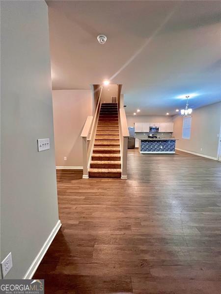 unfurnished living room featuring a chandelier, dark wood-style flooring, stairway, and baseboards