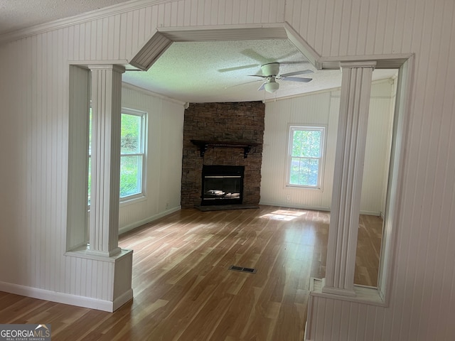 unfurnished living room featuring hardwood / wood-style floors, wood walls, crown molding, a fireplace, and a textured ceiling