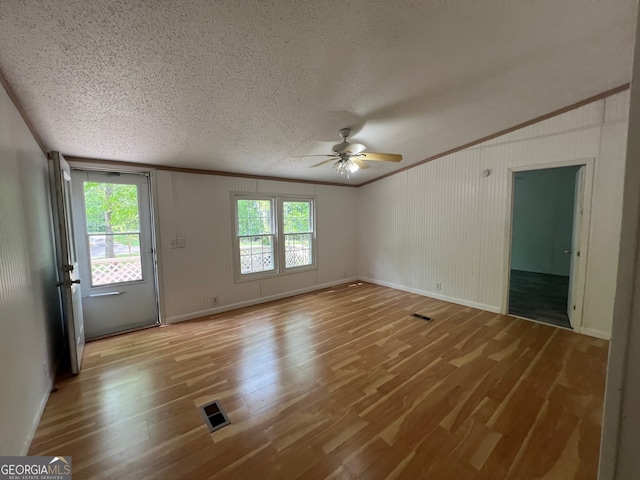 unfurnished living room featuring wood walls, light hardwood / wood-style flooring, ceiling fan, ornamental molding, and a textured ceiling