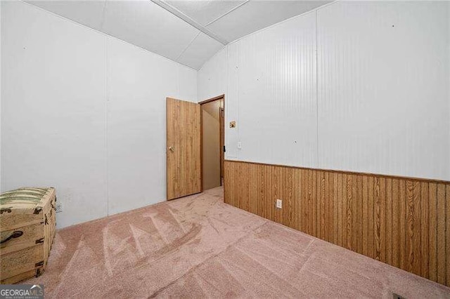 empty room with light carpet, lofted ceiling, and wood walls