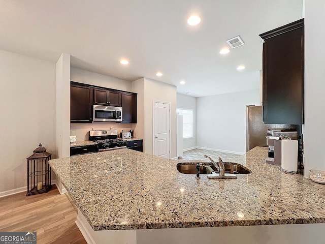 kitchen featuring sink, light hardwood / wood-style flooring, light stone countertops, kitchen peninsula, and stainless steel appliances