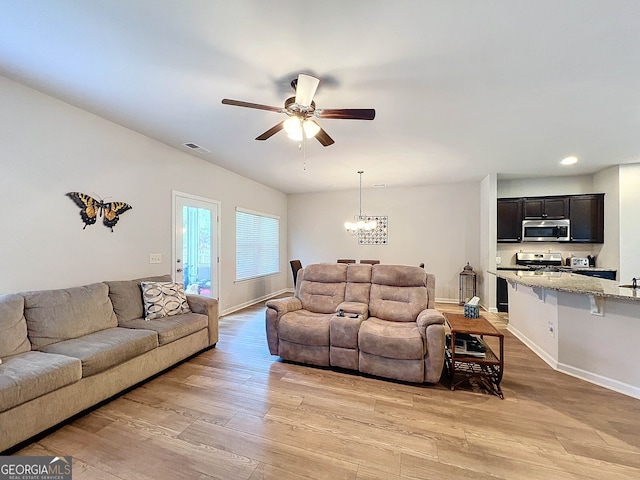 living room with ceiling fan with notable chandelier and light hardwood / wood-style flooring