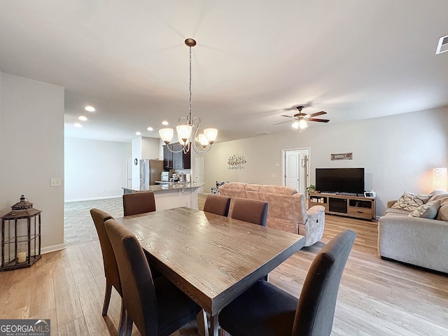 dining space with ceiling fan with notable chandelier and light wood-type flooring