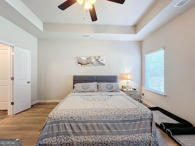 bedroom with light hardwood / wood-style floors, ceiling fan, and a tray ceiling