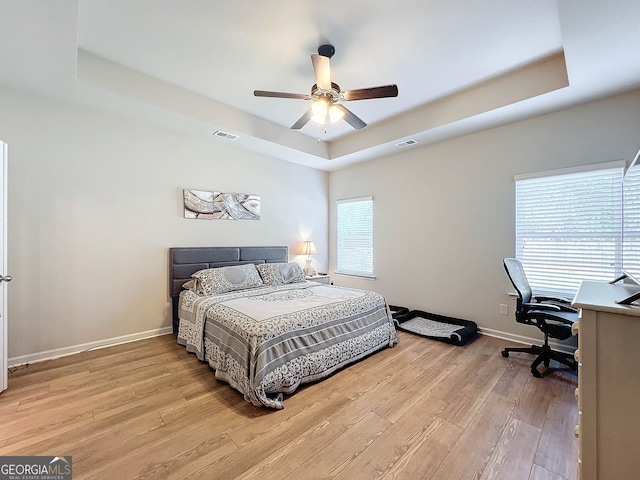 bedroom with a raised ceiling, light hardwood / wood-style flooring, and ceiling fan