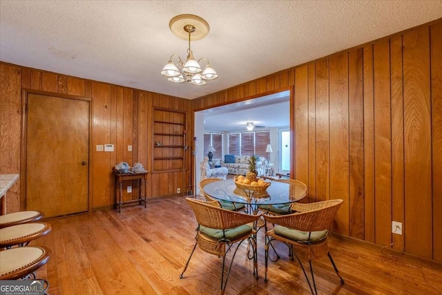 dining area with an inviting chandelier, wooden walls, built in features, light wood-type flooring, and a textured ceiling