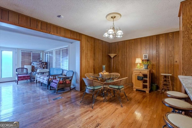 dining space featuring wooden walls, hardwood / wood-style floors, a textured ceiling, and an inviting chandelier