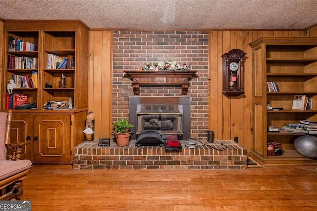 living room with a fireplace, a textured ceiling, hardwood / wood-style flooring, and wood walls