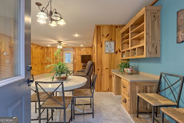 dining area with wooden walls and ceiling fan with notable chandelier