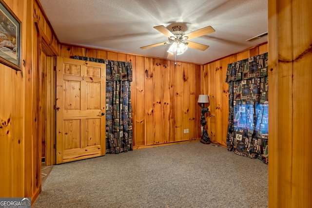 unfurnished room with carpet flooring, wooden walls, ceiling fan, and a textured ceiling