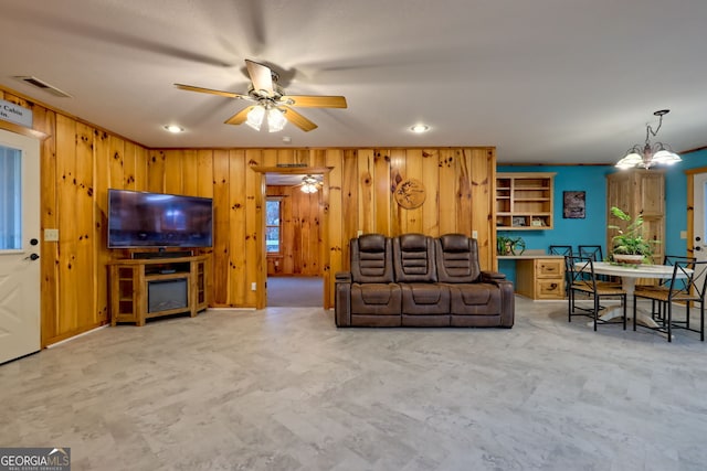 living room with ceiling fan with notable chandelier and wood walls