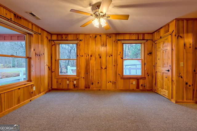 carpeted empty room with ceiling fan, wood walls, visible vents, baseboards, and ornamental molding