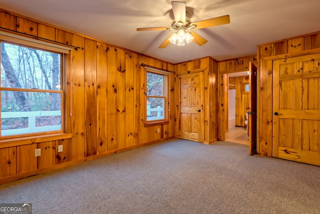 unfurnished bedroom with light carpet, multiple windows, wooden walls, and ceiling fan