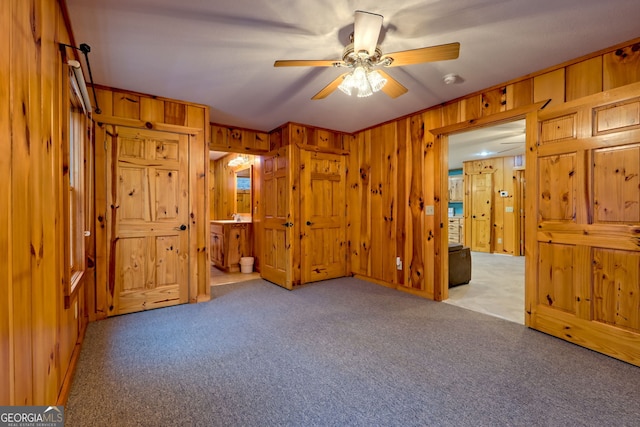 unfurnished bedroom with ensuite bathroom, wood walls, light colored carpet, and ceiling fan