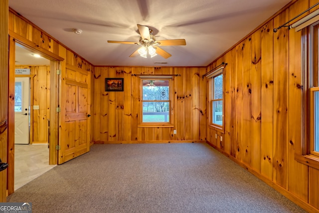 spare room featuring ornamental molding, carpet flooring, wooden walls, and a ceiling fan