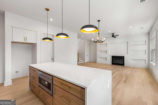 kitchen featuring white cabinets, decorative light fixtures, stainless steel microwave, and ceiling fan