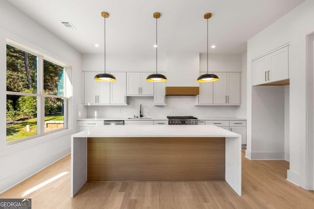 kitchen with light hardwood / wood-style flooring, white cabinetry, hanging light fixtures, and sink