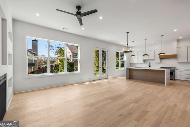 kitchen with hanging light fixtures, light wood-type flooring, stainless steel range, a kitchen island, and white cabinetry