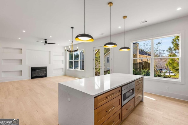 kitchen with ceiling fan with notable chandelier, pendant lighting, light hardwood / wood-style flooring, a center island, and stainless steel microwave