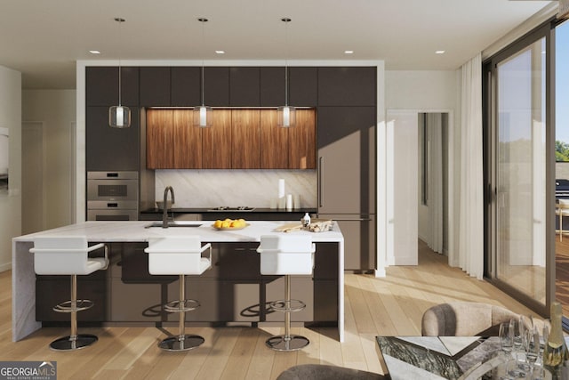 kitchen featuring a kitchen island with sink, sink, backsplash, and a kitchen bar