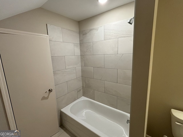 bathroom with toilet, lofted ceiling, and tiled shower / bath