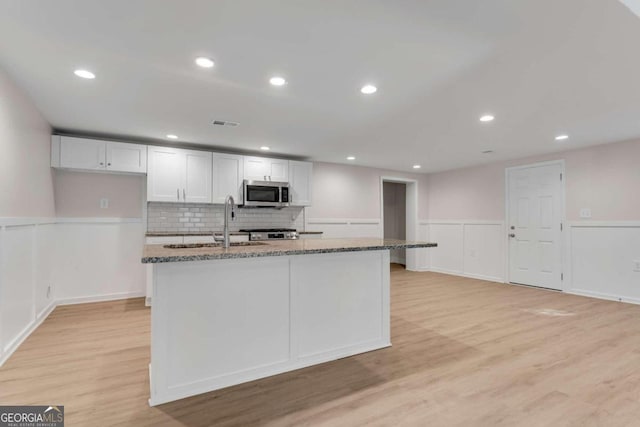 kitchen featuring dark stone counters, white cabinetry, stainless steel appliances, and light hardwood / wood-style floors