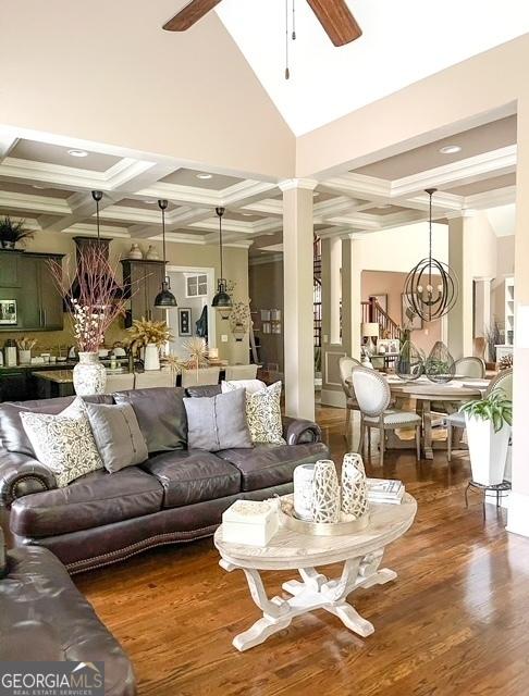 living room featuring beamed ceiling, ceiling fan with notable chandelier, ornate columns, and dark wood-type flooring