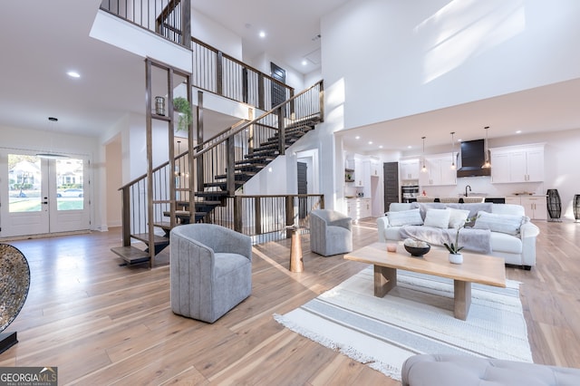 living room featuring light wood-type flooring, french doors, and a towering ceiling