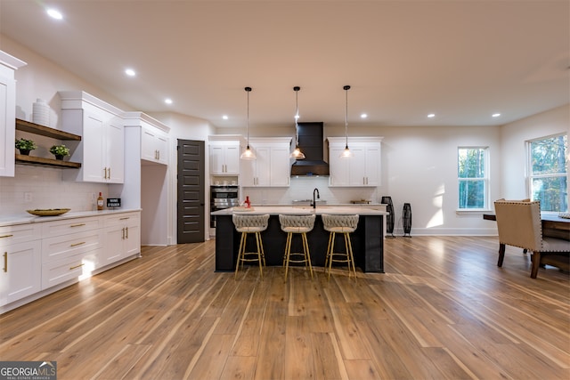 kitchen featuring white cabinets, an island with sink, light wood-type flooring, and custom exhaust hood