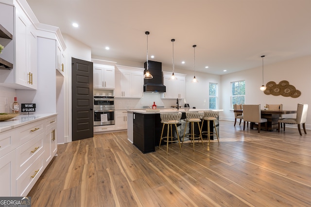 kitchen with premium range hood, double oven, white cabinets, and light hardwood / wood-style floors