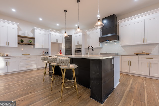 kitchen featuring light hardwood / wood-style floors, white cabinetry, custom range hood, and an island with sink