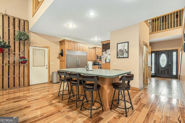 kitchen featuring light hardwood / wood-style floors, a breakfast bar area, appliances with stainless steel finishes, and an island with sink