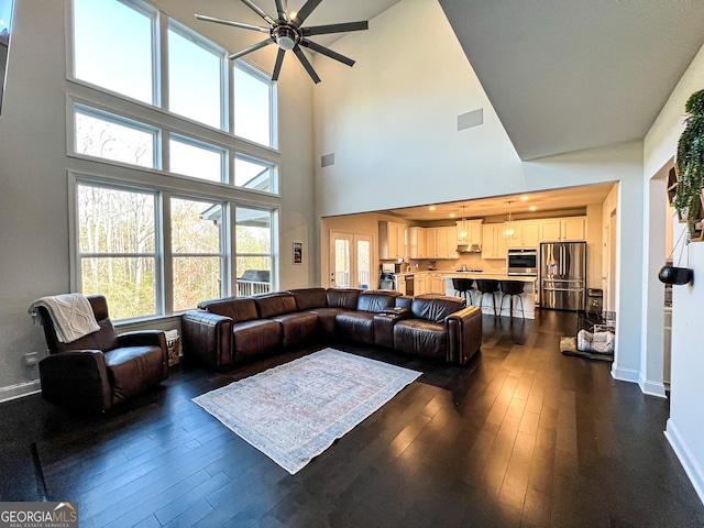 living room featuring a towering ceiling, ceiling fan, and dark wood-type flooring