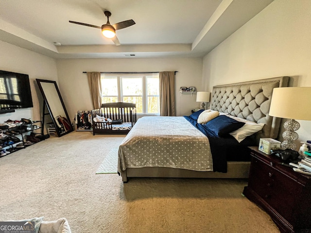 bedroom with a raised ceiling, ceiling fan, and carpet flooring