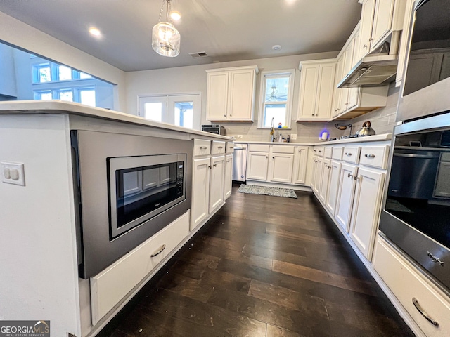 kitchen with backsplash, stainless steel dishwasher, pendant lighting, white cabinets, and oven